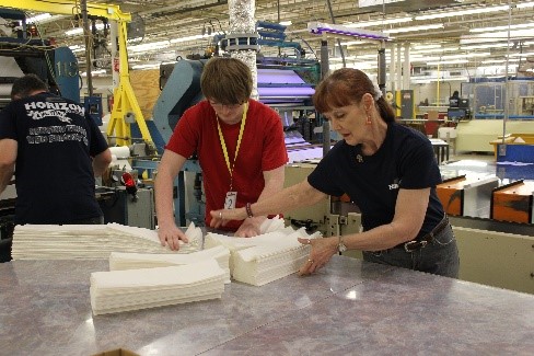 student working alongside plant employee breaking paper in manufacturing facility